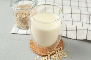 Glass of oat milk, oatmeal seeds, napkin on grey background, space for text. Closeup