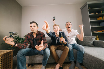 Company of friends is excited to playing video games. Guy is emotionally celebrating the victory over his friend in the console game. Video game and leisure concept