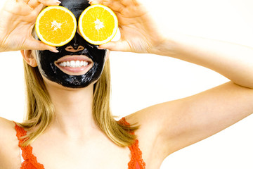 Girl black carbo mask on face holds orange fruit