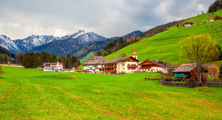 Fototapeta na wymiar Landscape in the Alps with mountain chalets and green meadows, Dolomite Alps, Italy.