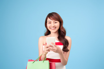 Beautiful young woman is using a smart phone for shopping online isolated on blue background studio