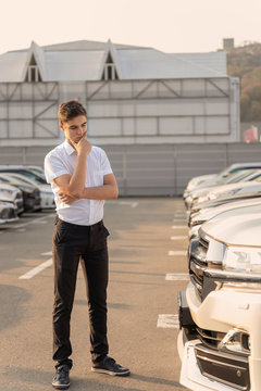 Teenager standing and thinking of choosing a new car at the dealership. Buying a vehicle in a car show