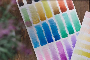 Artist painted watercolour swatch palette on wooden workstation background - Flat lay overhead view of various colour swatches used for color matching - spectrum, creative and artistic concepts