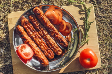 Sausages cooking on grill served on a plate with spices, herbs and tomatoes. Food background with barbecue party, top view - 305420738