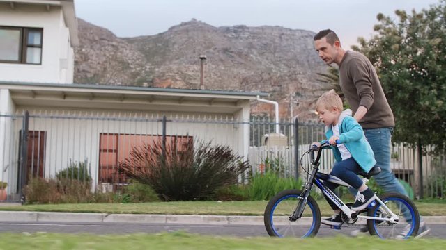 Father running teaching his son how to cycle ride a bicycle, helping balance