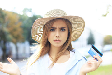 Cheerful young optimistic girl standing outdoors, holding credit card in hand.