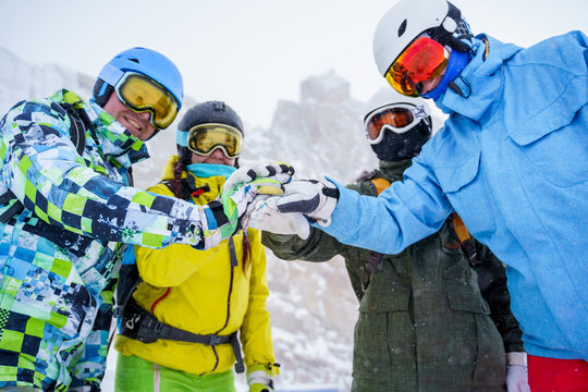 Photo of four happy snowboarders in helmet doing handshake at snow resort.