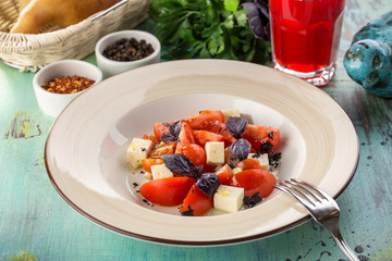 tomato salad with feta cheese and basil and glass of red drink on blue wooden table