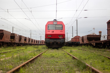 Fototapeta na wymiar Red and black locomotive train in track surrounded by freight wagons. Symmetry. Transport