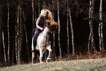 Reiterin galoppiert ohne Sattel mit ihrem Pony glücklich über eine Wiese mit Wald im Hintergrund