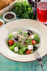 Fresh Greek salad with olives, tomato, feta cheese, cucumber and onion and glass of red drink on blue wooden table