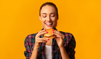 Joyful Young Woman Eating Burger Standing In Studio