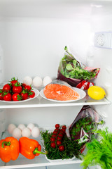Healthy food in the fridge The white fridge is full of proper food. Mediterranean diet, keto diet. Shelf with vegetables and red fish. Chilled Salmon with Herbs, Peppers and Cherry Tomatoes