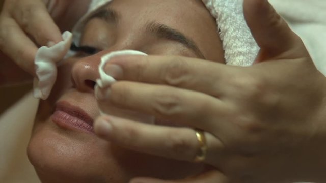 A woman having a skin care, the specialist cleaning her face with two cotton pads
