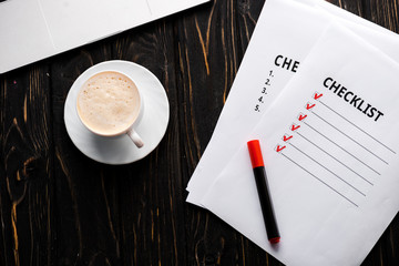 top view of papers with checklist and red marker pen near cup of coffee on table