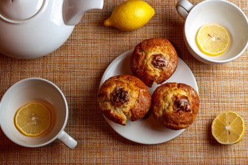 white teapot and two white cups of tea with lemon and muffins top view