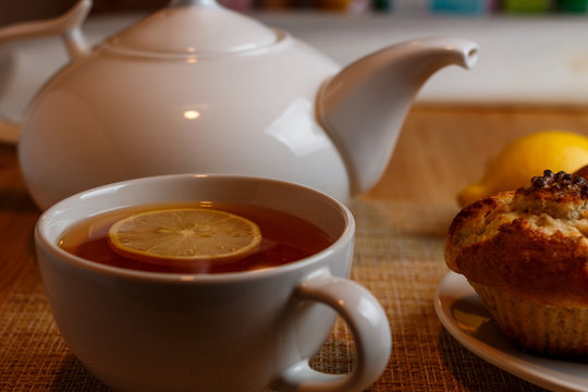 white teapot and two white cups of tea with lemon and muffins 
