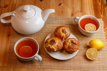 teapot is white and two white cups of tea with lemon and muffins