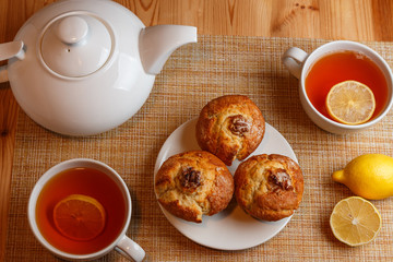 white teapot and two white cups of tea with lemon and muffins top view