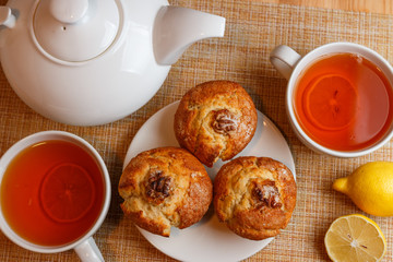 teapot is white and two white cups of tea with lemon and muffins