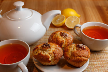 teapot is white and two white cups of tea with lemon and muffins