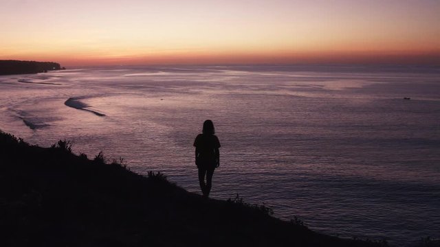 Silhouette of a woman standing on a hill watching a stunning sunset over the ocean in Bali. 