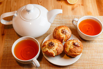 teapot is white and two white cups of tea with lemon and muffins