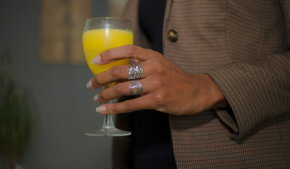 Black woman holding a glass of natural orange juice at work. Closeup and selective focus on her hand.