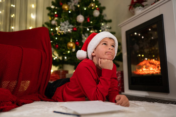 the boy lies under the Christmas tree near the fireplace and writes a letter to Santa Claus