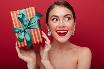 Positive woman with bright red lipstick holding present gift box.