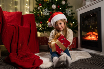 girl near the christmas tree and fireplace opens gifts