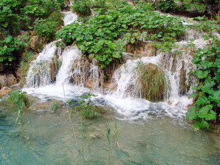 Top view of falling water into a crystal clear lake on a mountain slope richly covered with tall grass.