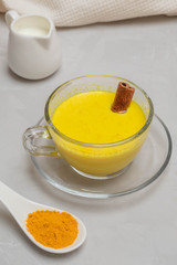 Glass cup of ayurvedic drink golden turmeric milk with curcuma powder, cinnamon stick and milk