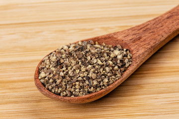 Spoon full of ground black pepper on a wooden background