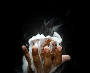 Hand smoke from dry ice in a bowl, black background.