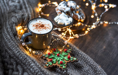 Cup of coffee with cinnamon. Christmas background with lights, warm knitted scarf.
