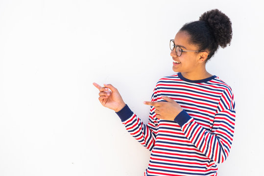 smiling african american teenage girl with glasses pointing fingers to copy space white background