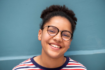 Close up of smiling young mixed race girl with glasses against blue wall