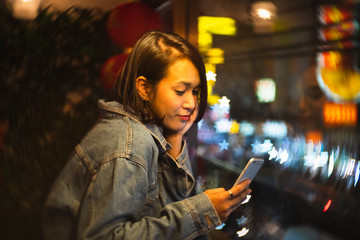 Young lifestyle stylish Asian woman using smartphone in Chinese restaurant at night, Attraction cool girl read message on mobile phone, Asia business people check something new on cellphone after work