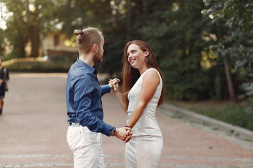 Fototapeta premium Cute couple in a park. Lady in a white dress. Man in a blue shirt