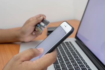 A man hand holding a credit card using a mobile and laptop to shopping online. Soft focus of young man of working using a laptop, Business concept, and communication technology. white blank screen