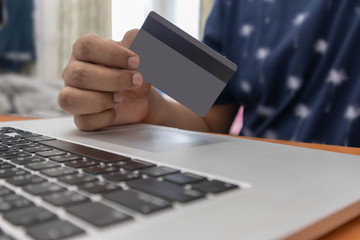 A man hand holding a credit card using a laptop to shopping online. Soft focus of young man of working using a laptop, Business concept, and communication technology.