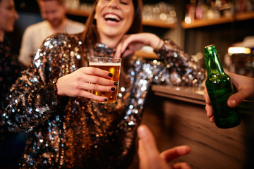 Beautiful caucasian smiling stylish woman  holding beer and chatting with friends. In background is bar counter. Pub interior.