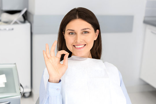 Satisfied pretty parient in dentist chair showing okay