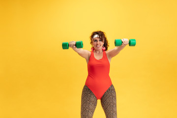 Young caucasian plus size female model's training on yellow background. Copyspace. Concept of sport, healthy lifestyle, body positive, fashion, style. Flexible woman with weights, looks stylish.