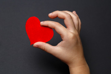 Fototapeta premium Children's hands hold a red heart on a black background, healthcare, love, organ donation, family insurance and CSR concept, World Heart Day, World Health Day, World Volunteer Day.