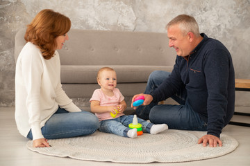 Little girl collects a pyramid with grandparents at living room. Happy family spend time together indoor, livestile