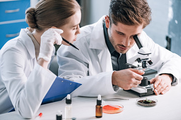 attractive biochemist near coworker looking through microscope