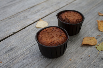 two chocolate cupcakes in paper molds on a wooden table