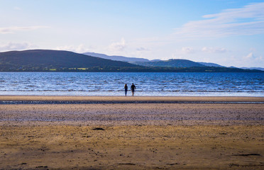 Fototapeta na wymiar Couple Walking on Beach with Sunset Reflection on the Sea. Blue Sky & Cloud at Background
